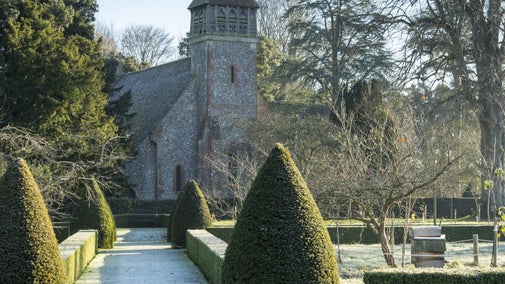 Frost covered grass path lined by topiary and box hedging in winter, with church and trees behind, Hinton Ampner, garden, Hampshire